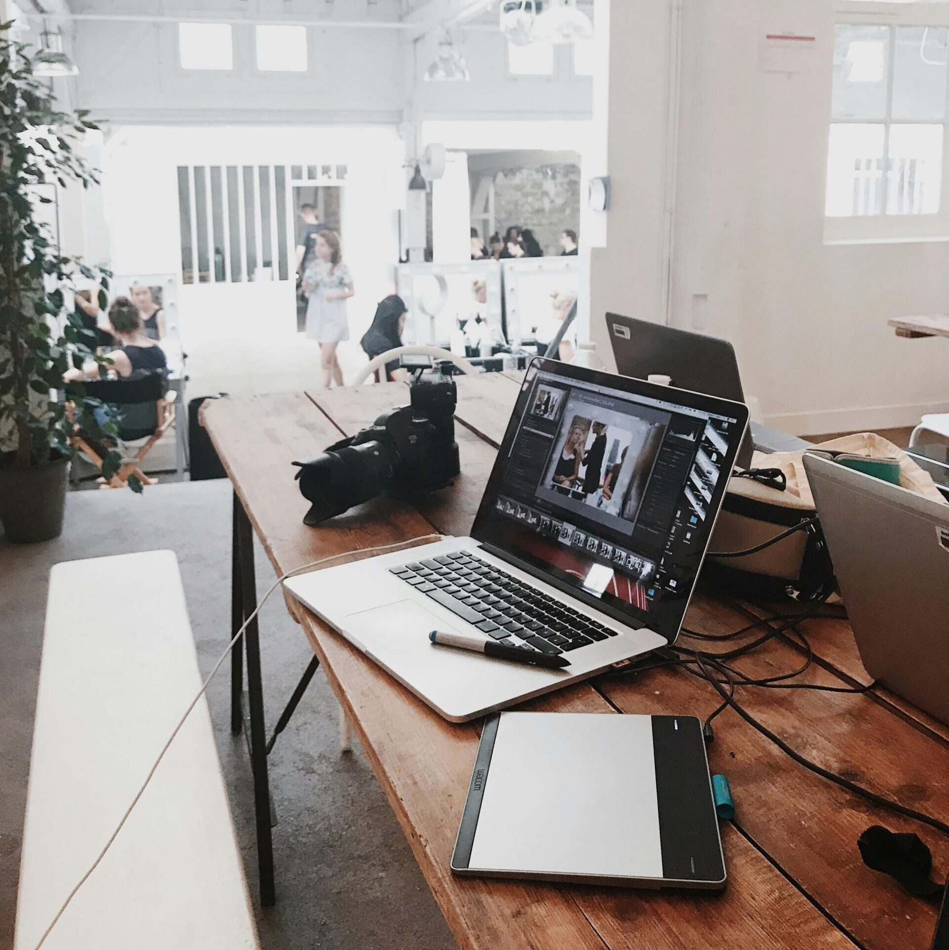 A bright, modern workspace featuring laptops, a camera, and a drawing tablet in an indoor office.
